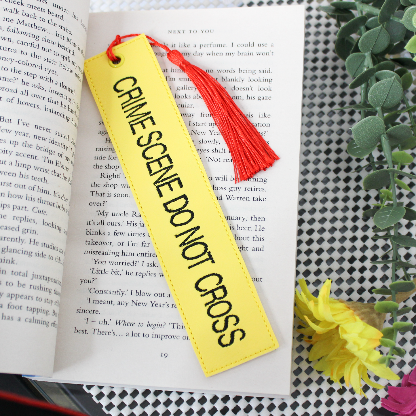 Yellow bookmark with 'CRIME SCENE DO NOT CROSS' text on an open book with a red tassel.
