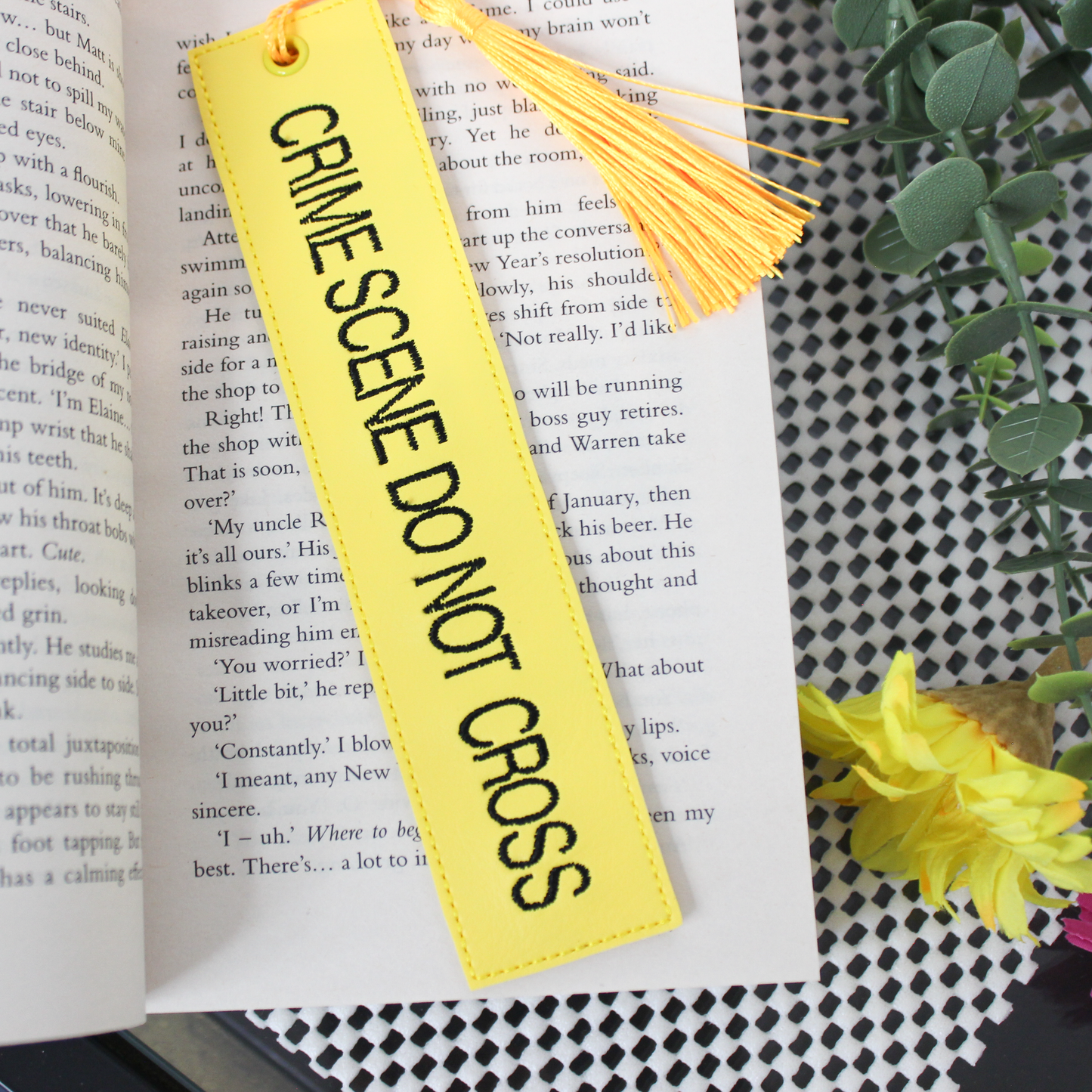 Yellow bookmark with 'CRIME SCENE DO NOT CROSS' text on an open book.