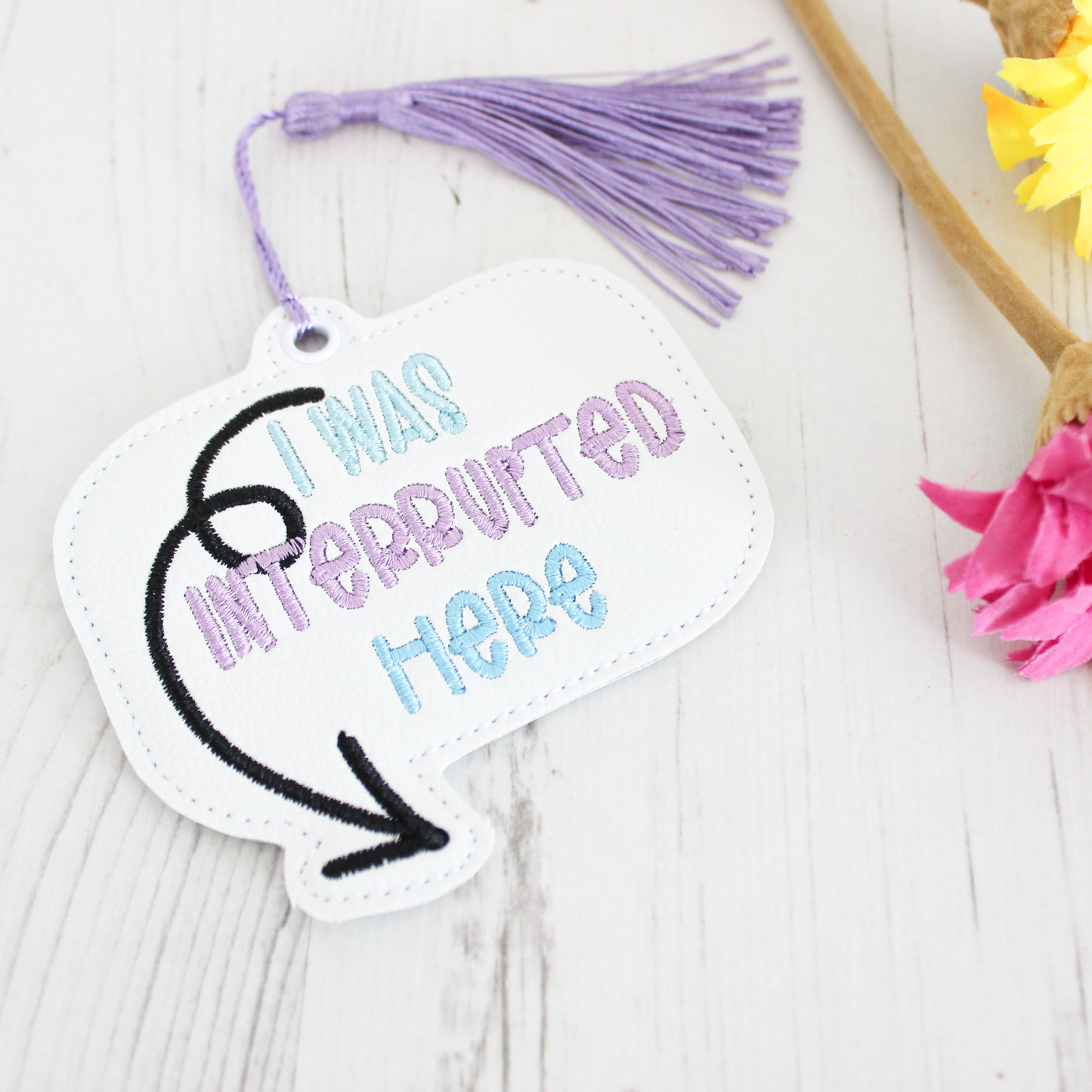 Decorative tag with 'I was interrupted here' text and tassel on a white background