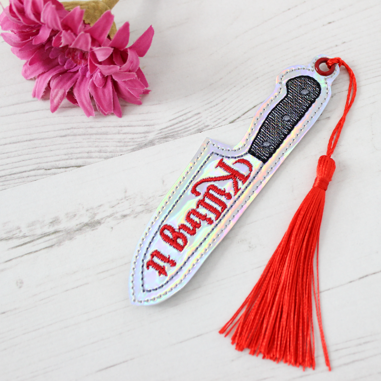 Novelty Knife shaped bookmark with a red tassel on a white surface with pink flowers.