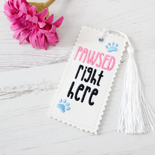 Bookmark with 'PAWSED right here' text and tassel on a white background