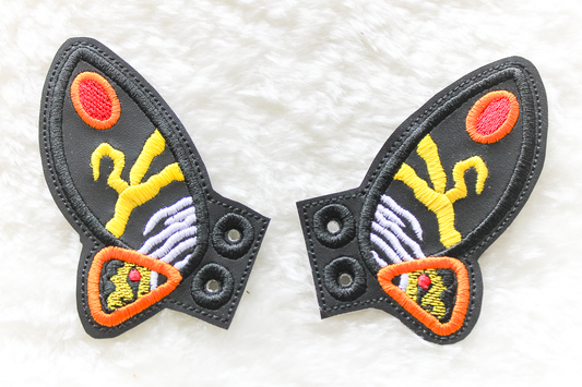Two decorative patches with a stylized Mothra design on a white background