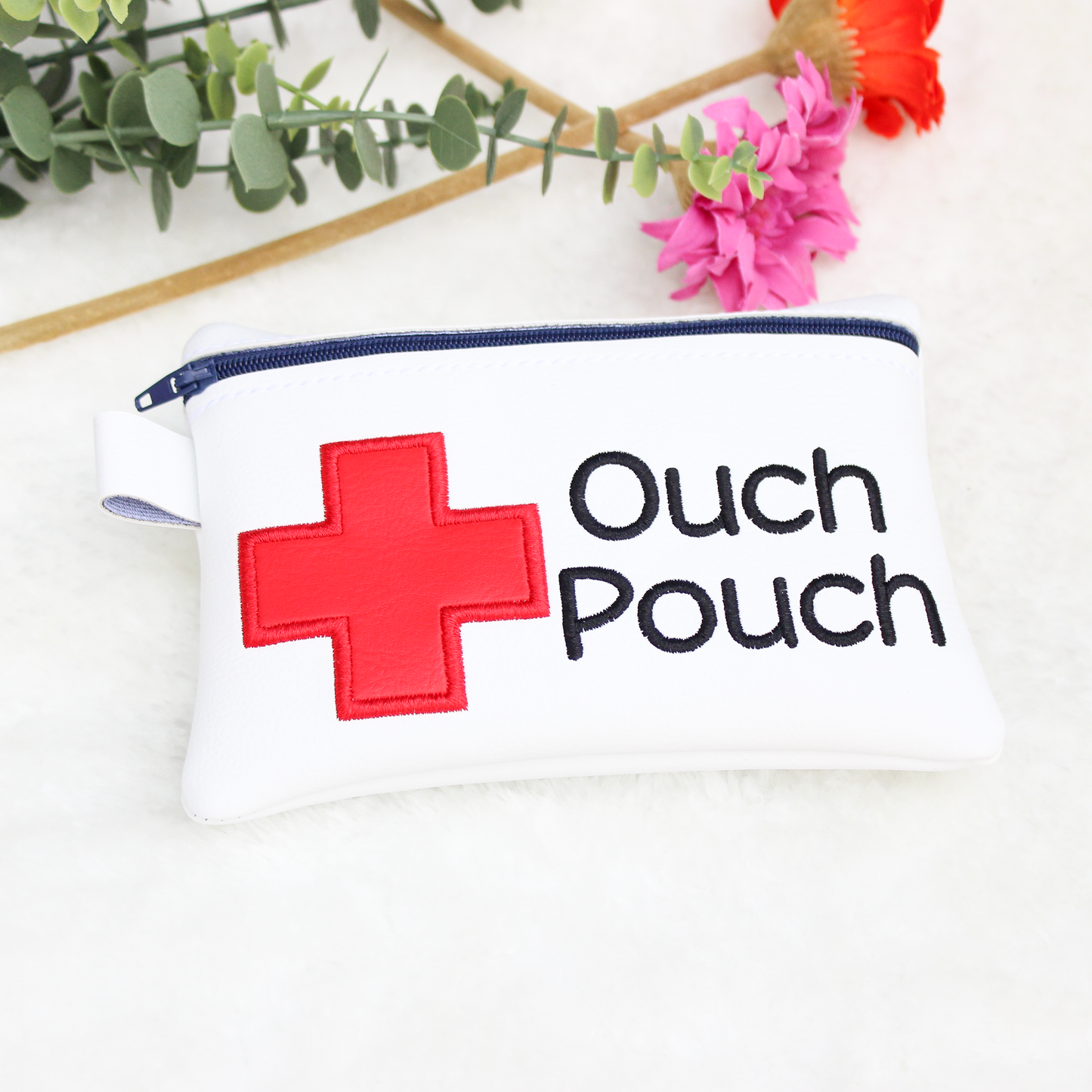 White pouch with red cross and 'Ouch Pouch' text on a white background with flowers.