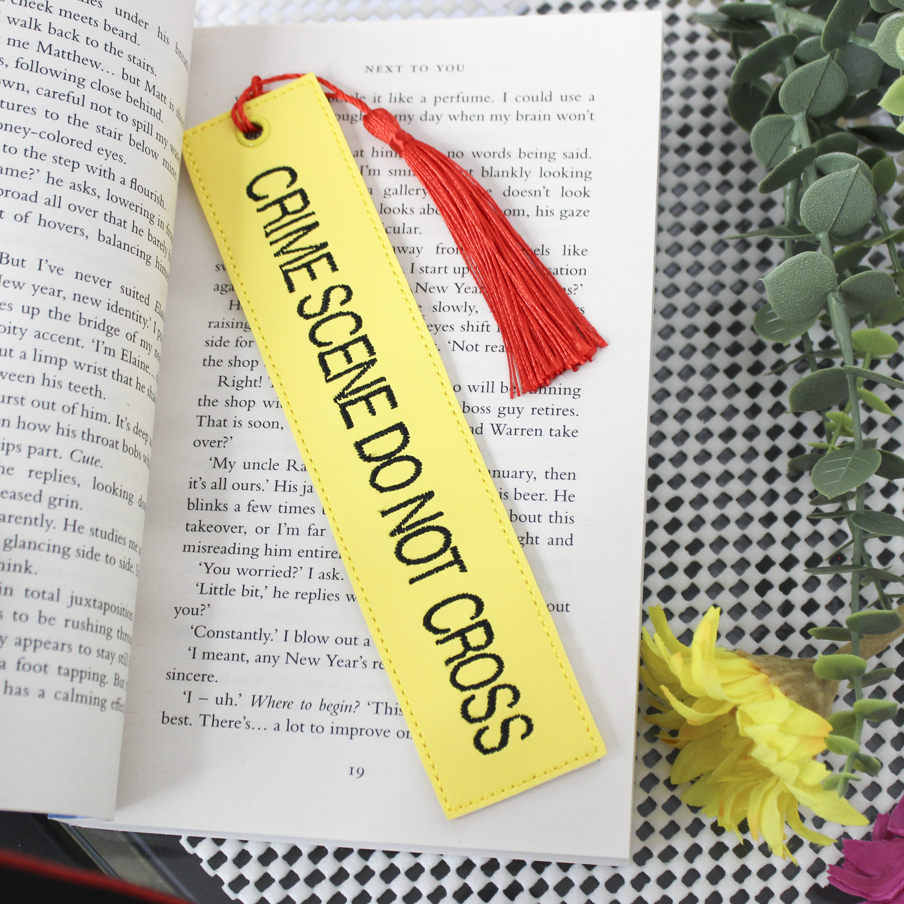 Yellow bookmark with 'CRIME SCENE DO NOT CROSS' text on an open book with a red tassel.