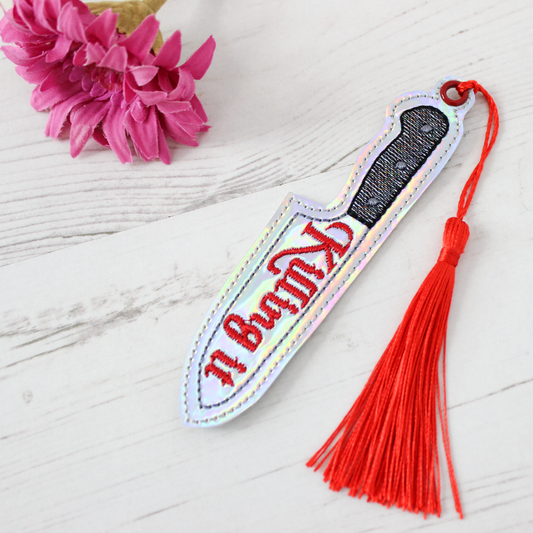 Novelty Knife shaped bookmark with a red tassel on a white surface with pink flowers.
