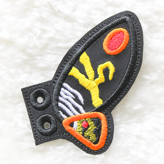 Embroidered Mothra shoe wings patch with colourful design on a white fluffy background